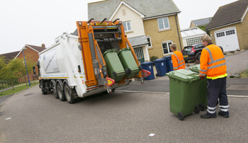 A bin collection lorry emptying two green bins